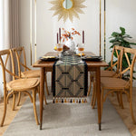 Une magnifique table à manger avec des chaises en bois, une décoration murale dorée et un chemin de table aux motifs géométriques noirs et blancs, créant une ambiance chaleureuse et élégante.