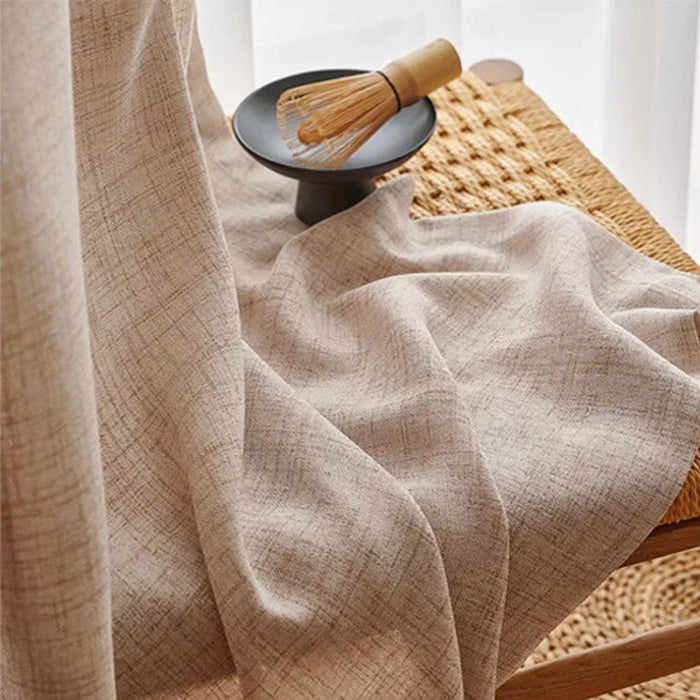 Gros plan sur un rideau écru à motif croisé, posé sur une chaise tressée avec un fouet à thé matcha en décoration.