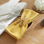 Une serviette de table jaune dorée, délicatement enroulée et attachée avec une ficelle, posée sur une table en bois avec des couverts et une décoration florale, créant une ambiance chaleureuse et accueillante.