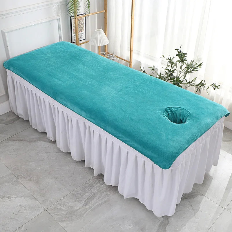 Lit de massage confortable et relaxant avec un drap blanc et un oreiller turquoise, entouré de plantes vertes dans une pièce lumineuse.
