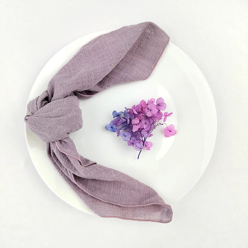Une écharpe grise élégante et délicate à côté d'une touffe de fleurs violettes et bleues sur un fond blanc.