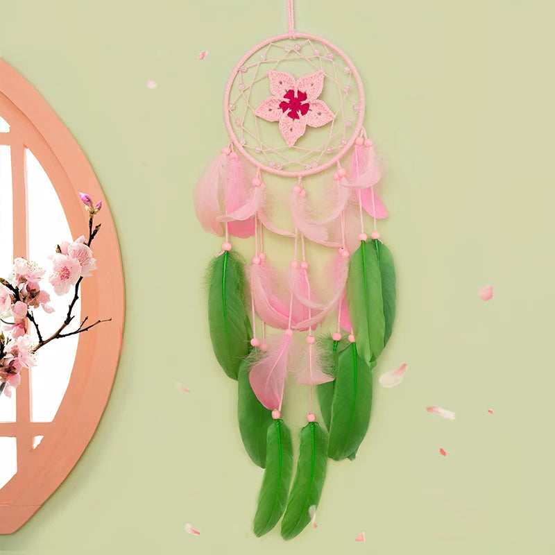 Attrape-rêves rose et vert délicat suspendu sur un mur vert clair avec des fleurs de cerisier en arrière-plan.
