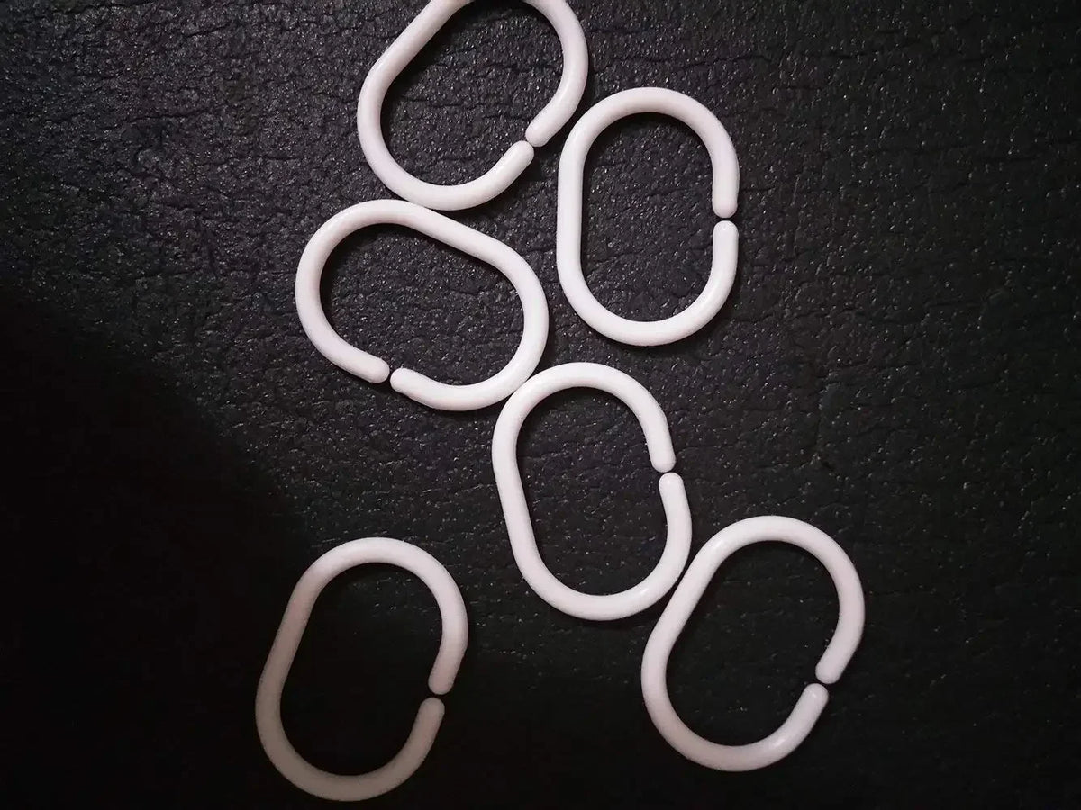 Ensemble d’anneaux de douche blancs de forme ovale, disposés sur un fond noir. 