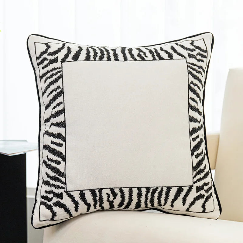 Coussin décoratif noir et blanc avec motif zébré encadrant une surface centrale vide.