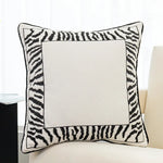 Coussin décoratif noir et blanc avec motif zébré encadrant une surface centrale vide.