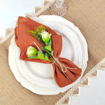 Une élégante décoration de table avec une serviette en tissu rouille et un bouquet de fleurs ornées.