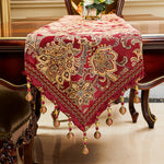 Chemin de table décoratif en velours rouge avec motifs floraux dorés et pompons.
