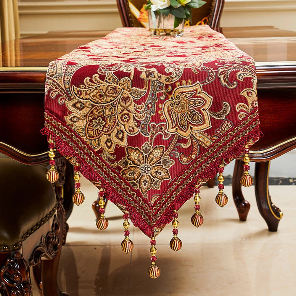 Chemin de table décoratif en velours rouge avec motifs floraux dorés et pompons.