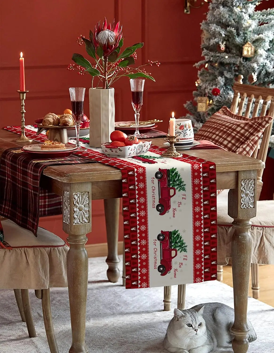 Une table de Noël richement décorée avec des touches de rouge, de vert et de blanc, avec un bouquet de fleurs spectaculaire, des bougies allumées et un chat endormi, dans un décor festif.