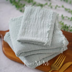 Serviettes de table en lin gris naturel, douces et texturées, posées sur un plateau en bois.