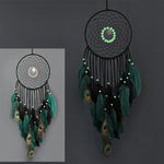Attrape-rêves décoratif noir et vert avec des plumes de paon, boules lumineuses et motif circulaire.