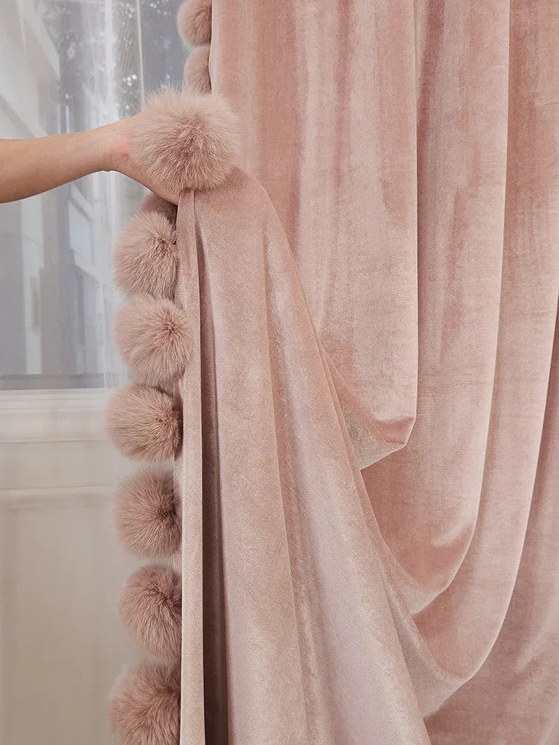 Zoom sur le rideau rose poudré en velours avec pompons moelleux cousus sur le bord, détail raffiné et chaleureux.