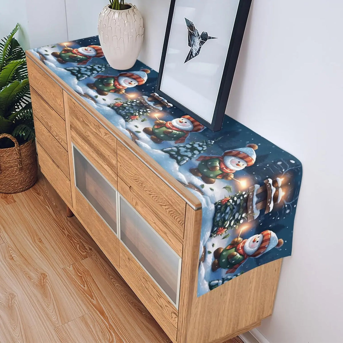 Cette image présente un meuble en bois clair décoré d'un motif de bonhommes de neige enneigés dans un paysage hivernal.