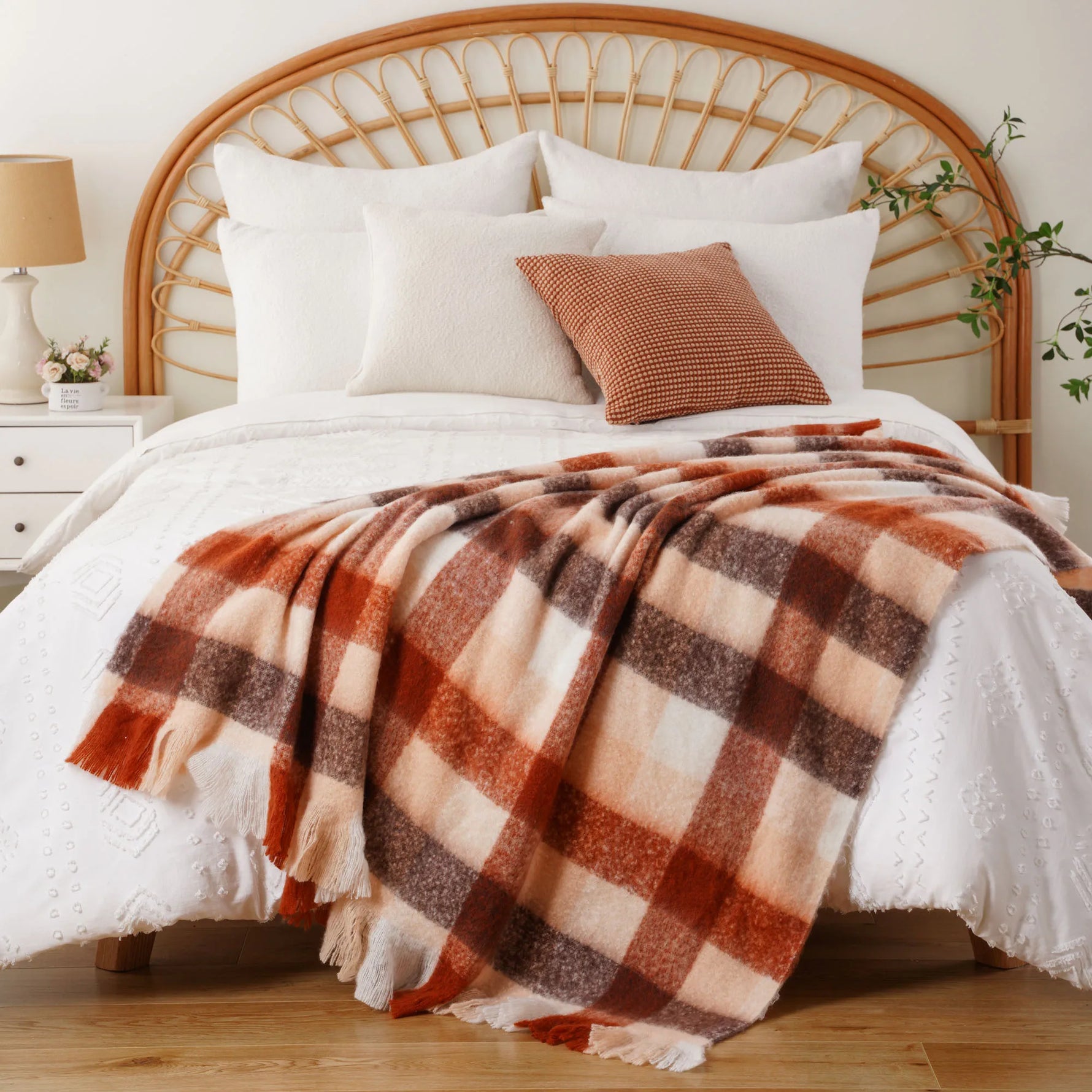 Un lit double au style rustique avec une tête de lit en rotin, une couverture à carreaux dans des tons chauds et des oreillers assortis pour une atmosphère cocooning.