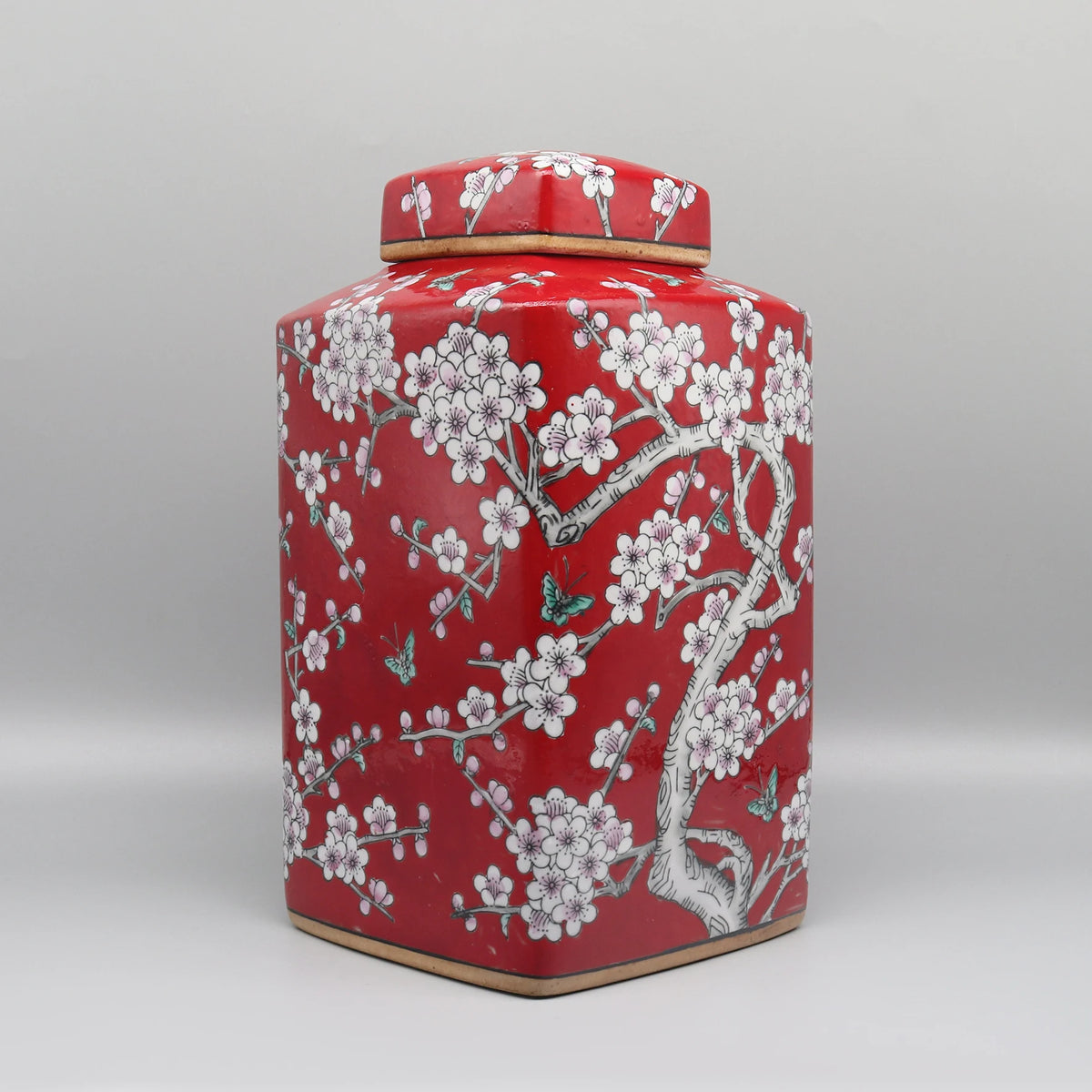 Un élégant pot de stockage en céramique de couleur rouge vif, décoré de magnifiques fleurs de prunier blanc et de papillons, évoquant une ambiance orientale chaleureuse et raffinée.