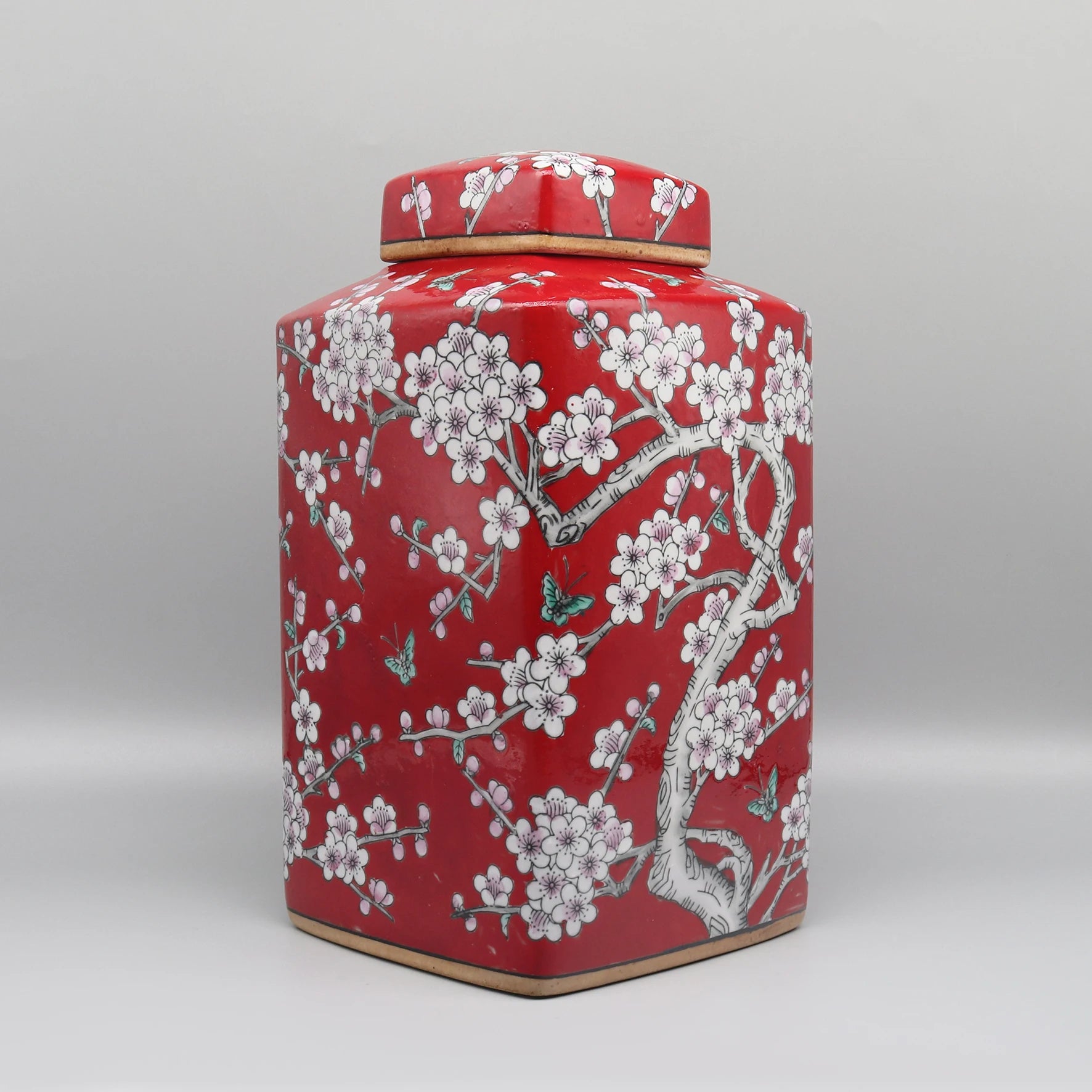 Un élégant pot de stockage en céramique de couleur rouge vif, décoré de magnifiques fleurs de prunier blanc et de papillons, évoquant une ambiance orientale chaleureuse et raffinée.