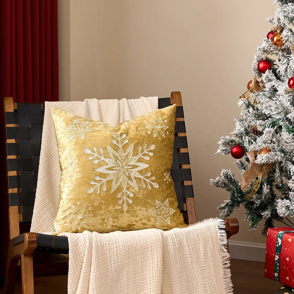 Coussin décoratif doré avec motif flocon de neige, posé sur une chaise en bois près d'un arbre de Noël décoré de boules rouges et d'ornements.