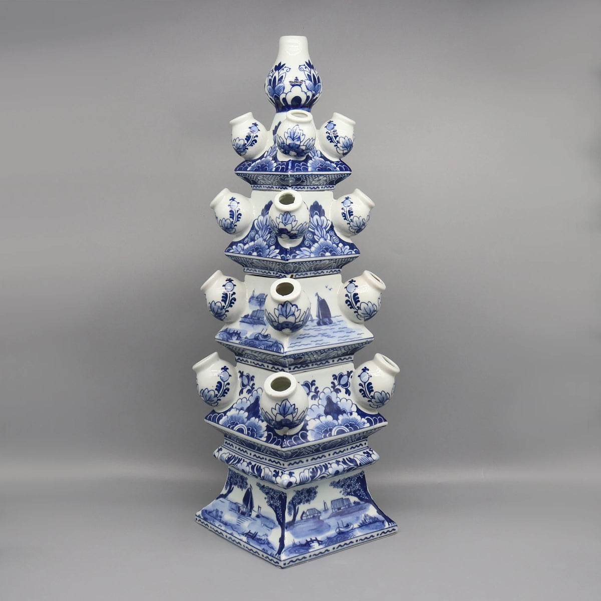 Cette image montre un objet en céramique bleu et blanc de style chinois, composé de plusieurs formes empilées les unes sur les autres, avec des motifs floraux et des scènes de paysage.