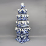 Cette image montre un objet en céramique bleu et blanc de style chinois, composé de plusieurs formes empilées les unes sur les autres, avec des motifs floraux et des scènes de paysage.