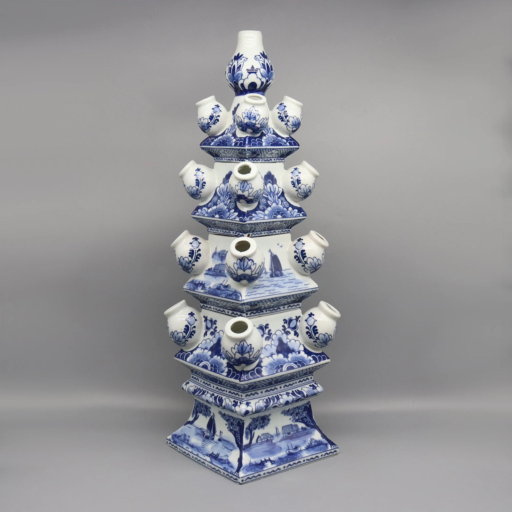 Cette image montre un objet en céramique bleu et blanc de style chinois, composé de plusieurs formes empilées les unes sur les autres, avec des motifs floraux et des scènes de paysage.