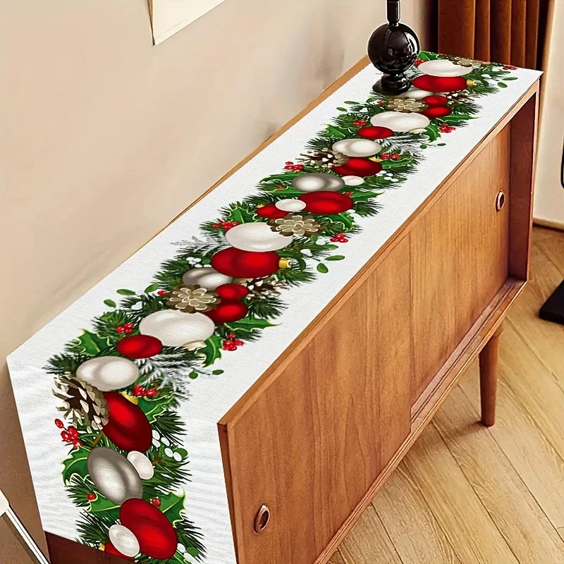 Chemin de table décoré avec une guirlande de Noël composée de branches de sapin, de boules rouges et blanches, de pommes de pin et de baies rouges sur un meuble en bois.