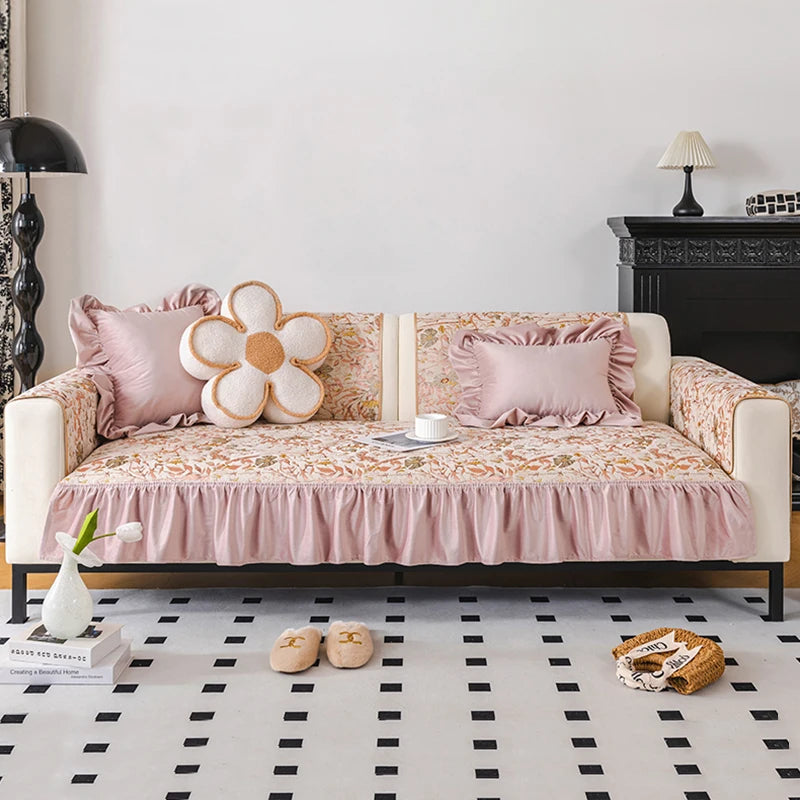 Canapé moderne capitonné rose avec coussin fleuri et accessoires décoratifs posé sur un sol carrelé noir et blanc dans un intérieur élégant.
