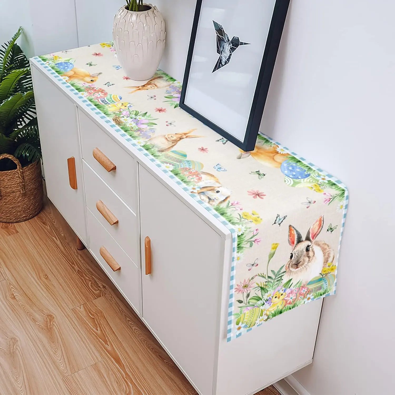 Commode blanche avec des tiroirs en bois et une décoration de motifs floraux et d'animaux mignons, placée devant une fenêtre et à côté d'une plante verte dans un vase.