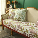 Un canapé en velours avec des coussins imprimés de motifs de feuillage, dans des tons verts et marrons, créant une ambiance chaleureuse et naturelle dans un intérieur.