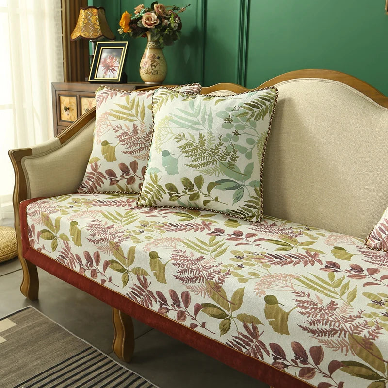 Un canapé en velours avec des coussins imprimés de motifs de feuillage, dans des tons verts et marrons, créant une ambiance chaleureuse et naturelle dans un intérieur.