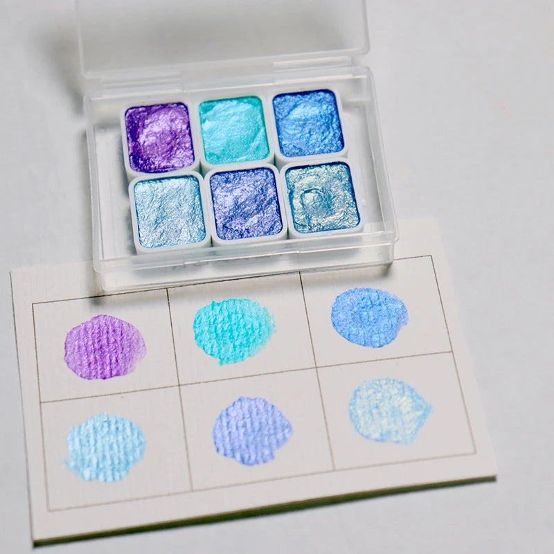 peintures aquarelle palette compacte bleu vert violet rose beige jaune blanc texture granuleuse opaques