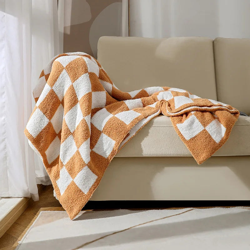 Une couverture en coton doux et texturée avec un motif géométrique en tons de beige et orange, disposée sur un canapé.