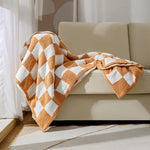Une couverture en coton doux et texturée avec un motif géométrique en tons de beige et orange, disposée sur un canapé.