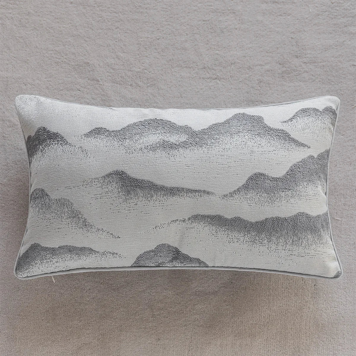 Coussin décoratif avec un motif de montagnes et de paysage brumeux, dans des tons de gris neutres, créant une ambiance apaisante et sereine.