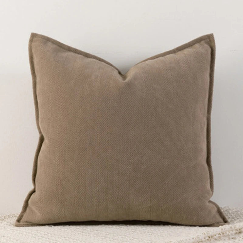 Coussin en lin beige, élégant et sobre, reposant sur une couverture blanche.