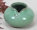 Un vase en céramique de couleur vert clair, avec un motif décoratif sur la surface.