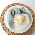 Une délicate rose blanche posée sur une assiette blanche entourée d'une nappe verte sur un plateau en osier tressé.