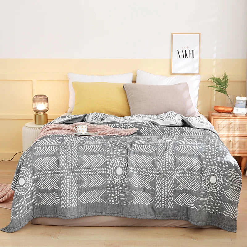 Un lit douillet avec une couverture grise ornée de motifs géométriques, placé dans une chambre lumineuse et chaleureuse aux murs jaunes.