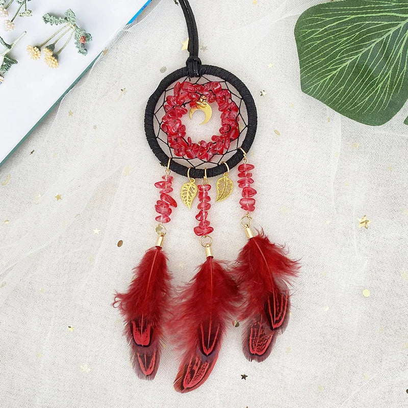 Un capteur de rêves rouge et or suspendu avec des plumes rouges, des cristaux rouges et une lune dorée.