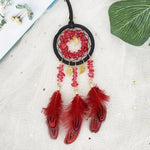 Un capteur de rêves rouge et or suspendu avec des plumes rouges, des cristaux rouges et une lune dorée.