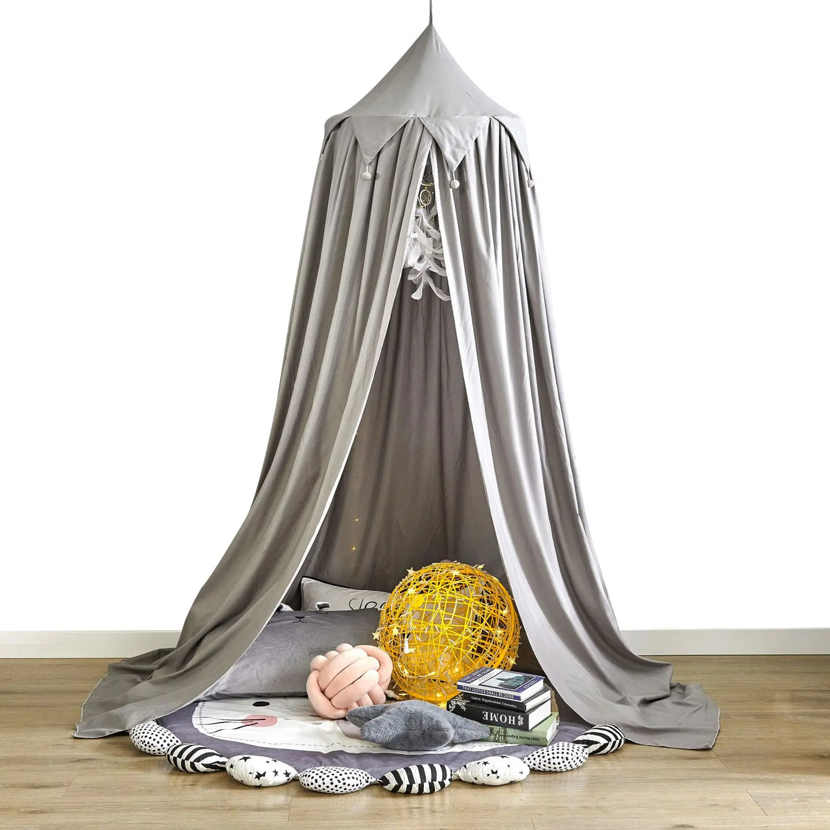 Un coin cocooning douillet et confortable, avec un dôme gris suspendu, des coussins moelleux, un gros ballon jaune et des livres, créant un espace intime et relaxant.