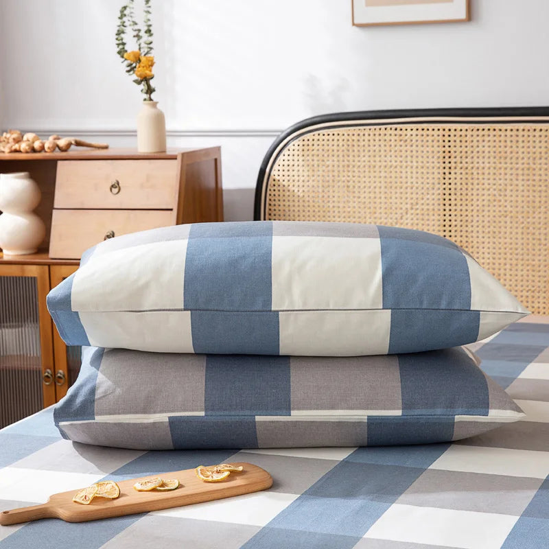 Des coussins décoratifs rayés de couleurs neutres posés sur un lit, avec un plan de travail en bois et un meuble vintage dans l'arrière-plan.