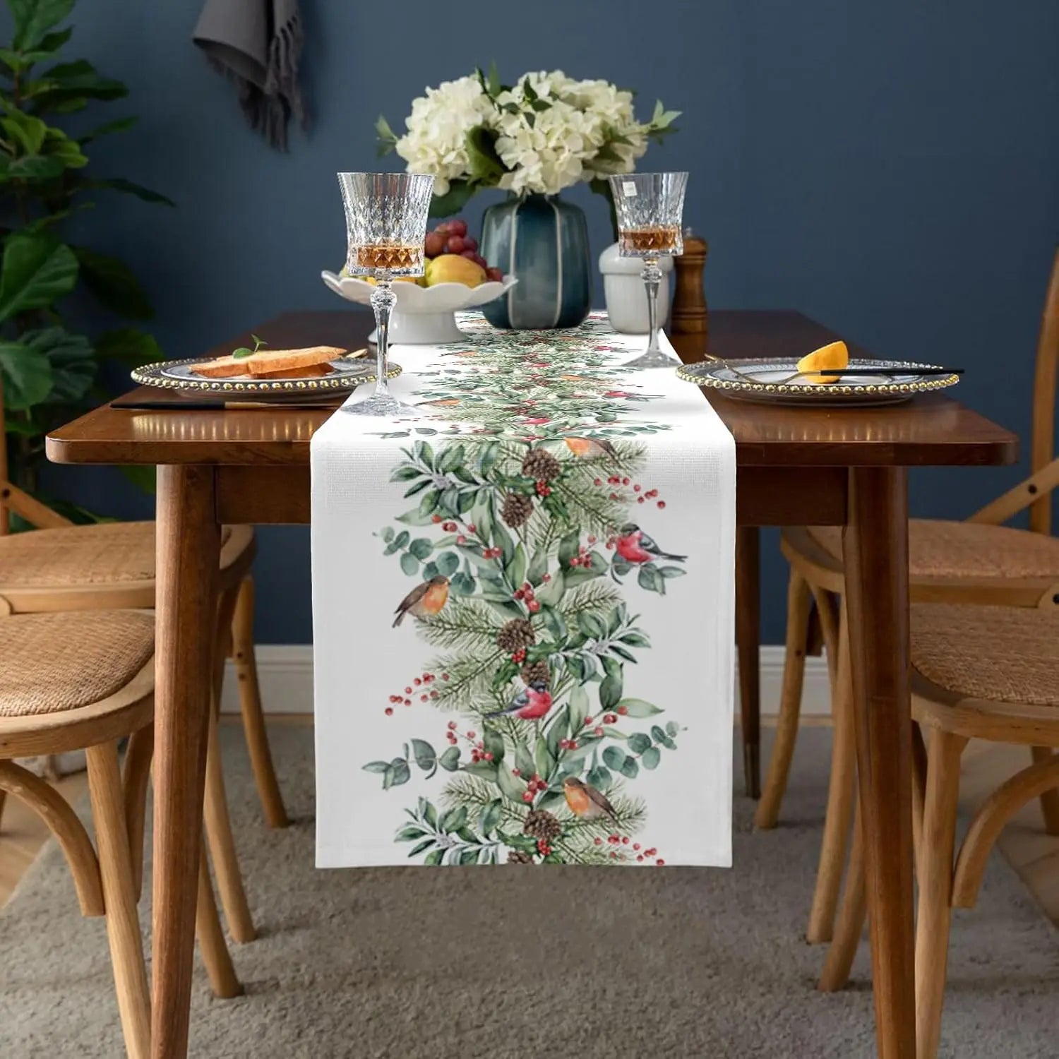 Sur une table élégante ornée de verres à vin et de fleurs blanches, un chemin de table décoré de motifs floraux et d'oiseaux crée une ambiance chaleureuse et festive.