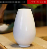 Vase blanc en céramique de taille moyenne sur une surface en bois, destiné à la décoration intérieure.