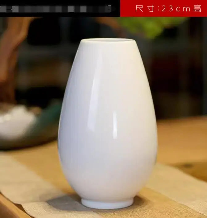 Vase blanc en céramique de taille moyenne sur une surface en bois, destiné à la décoration intérieure.