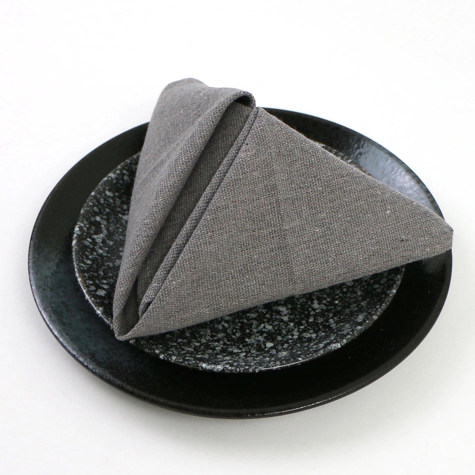 Un élégant pliage de serviette gris en textile, décoré avec soin sur un plat de service en céramique noire.