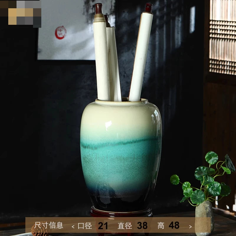 Un vase décoratif de couleur verte glaçurée avec des pinceaux blancs à l'intérieur, posé sur une surface en bois sombre.