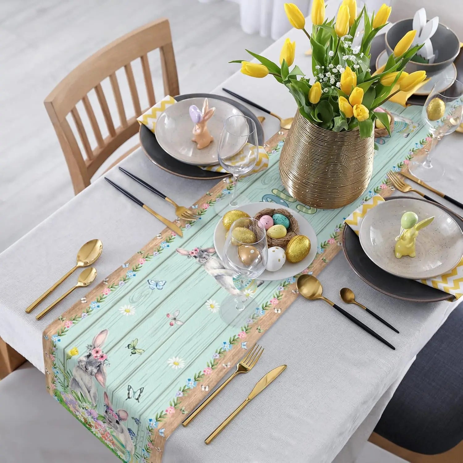 Une table de fête élégamment dressée avec de magnifiques fleurs de printemps, des décorations de Pâques et des couverts dorés.