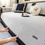 Une chambre lumineuse et épurée avec un lit aux draps rayés, des coussins noirs et blancs ainsi qu'un doux ours en peluche, le tout sur un tapis à motifs.