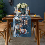 Décor de table élégant avec des fleurs blanches, des verres à vin et des fruits disposés sur une nappe bleue ornée d'un motif hivernal.
