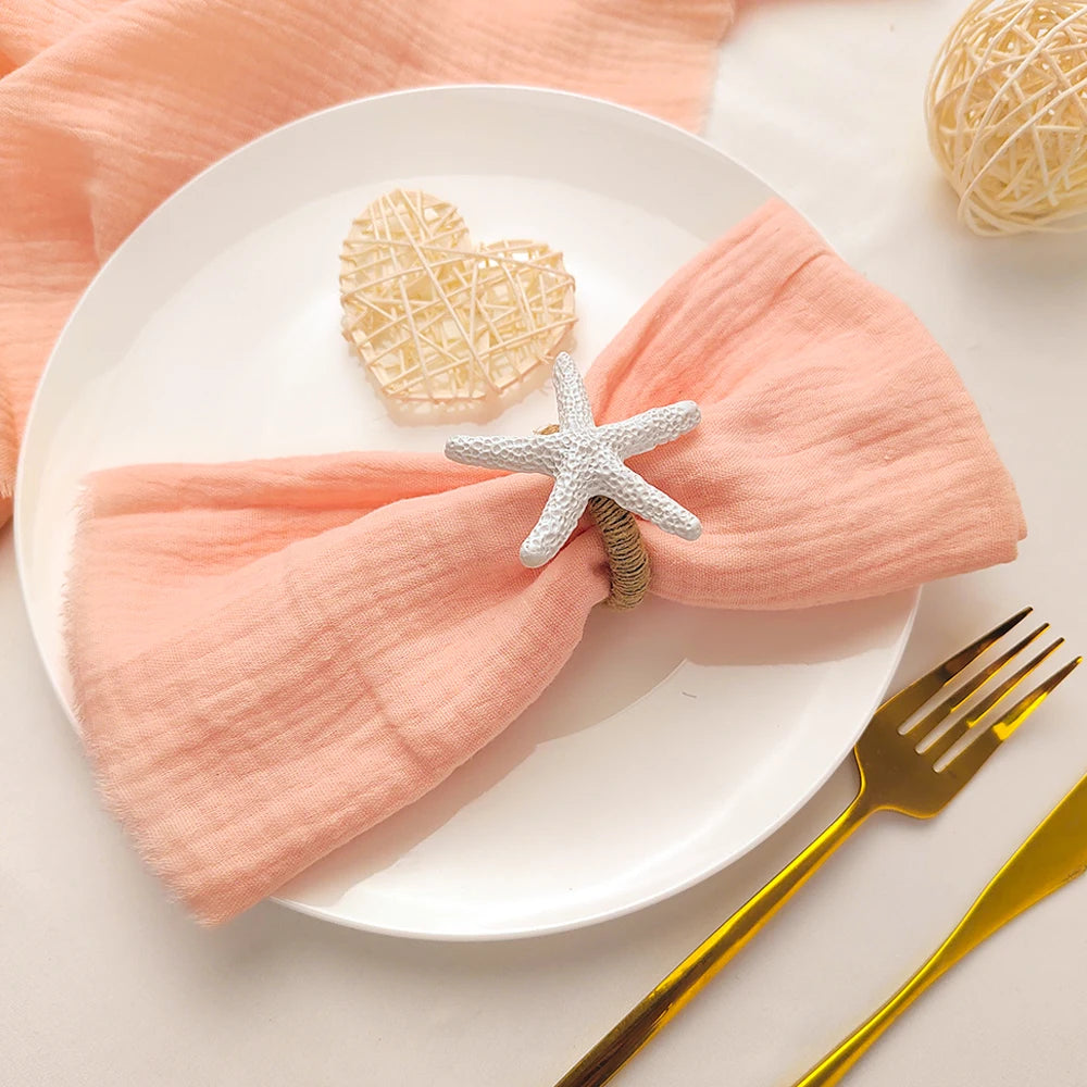 Une table de service décorée d'une serviette en lin rose pâle et d'un ornement en forme d'étoile de mer.